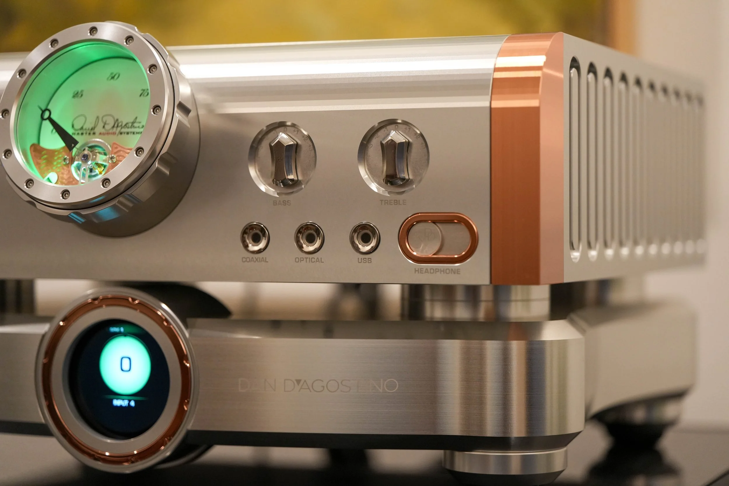 Close-up of a high-end audio amplifier with metallic finish, orange accents, and digital display, showing controls for bass, treble, and connectivity ports.