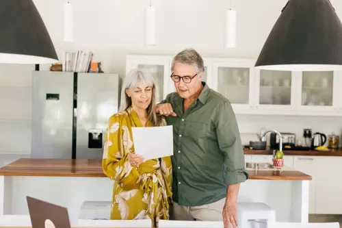 An elderly couple in a kitchen looking at a piece of paper together.