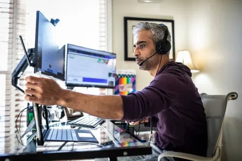 Man wearing headphones working at a multi-monitor computer setup in an office.