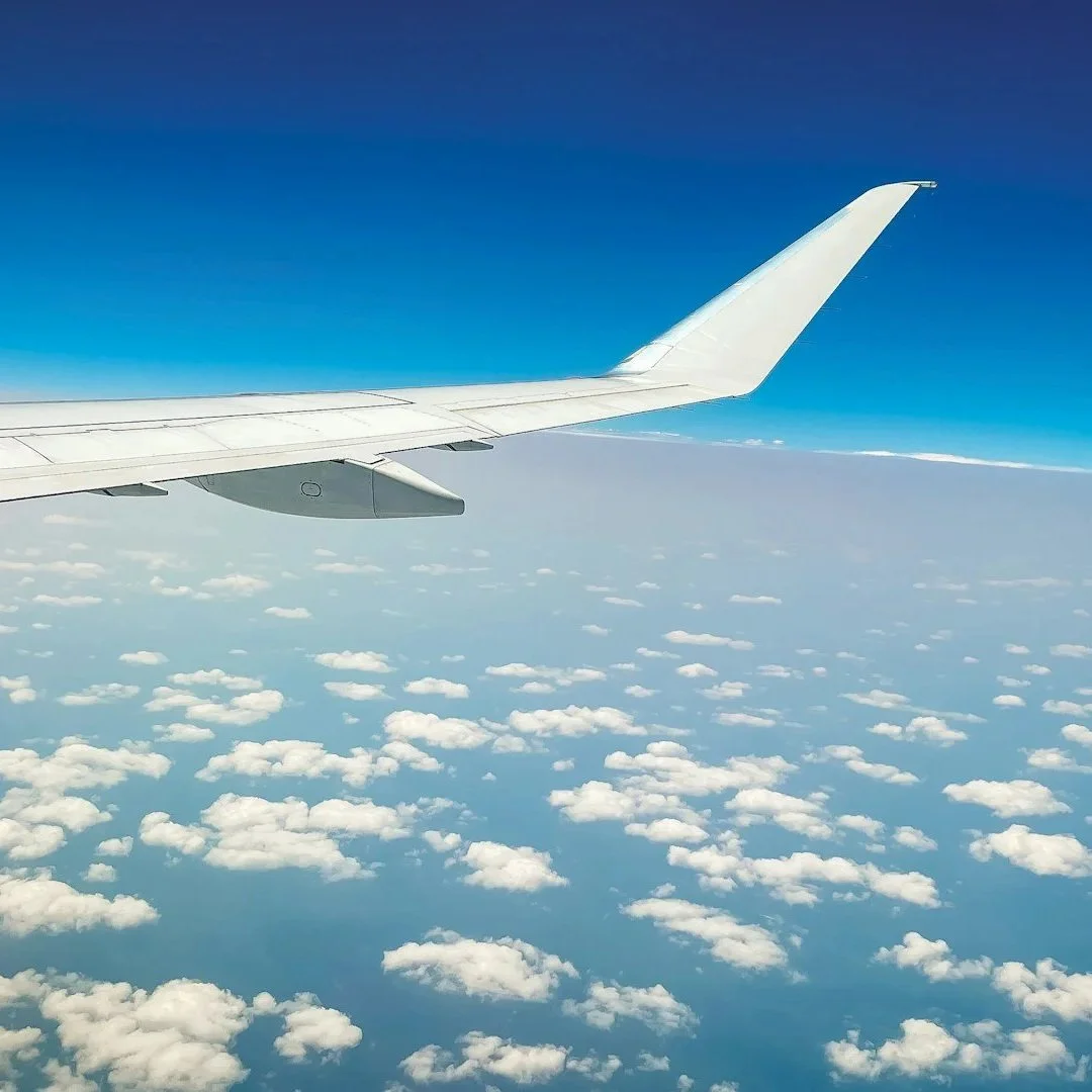View from an airplane window showing a white airplane wing and a sky with scattered clouds.