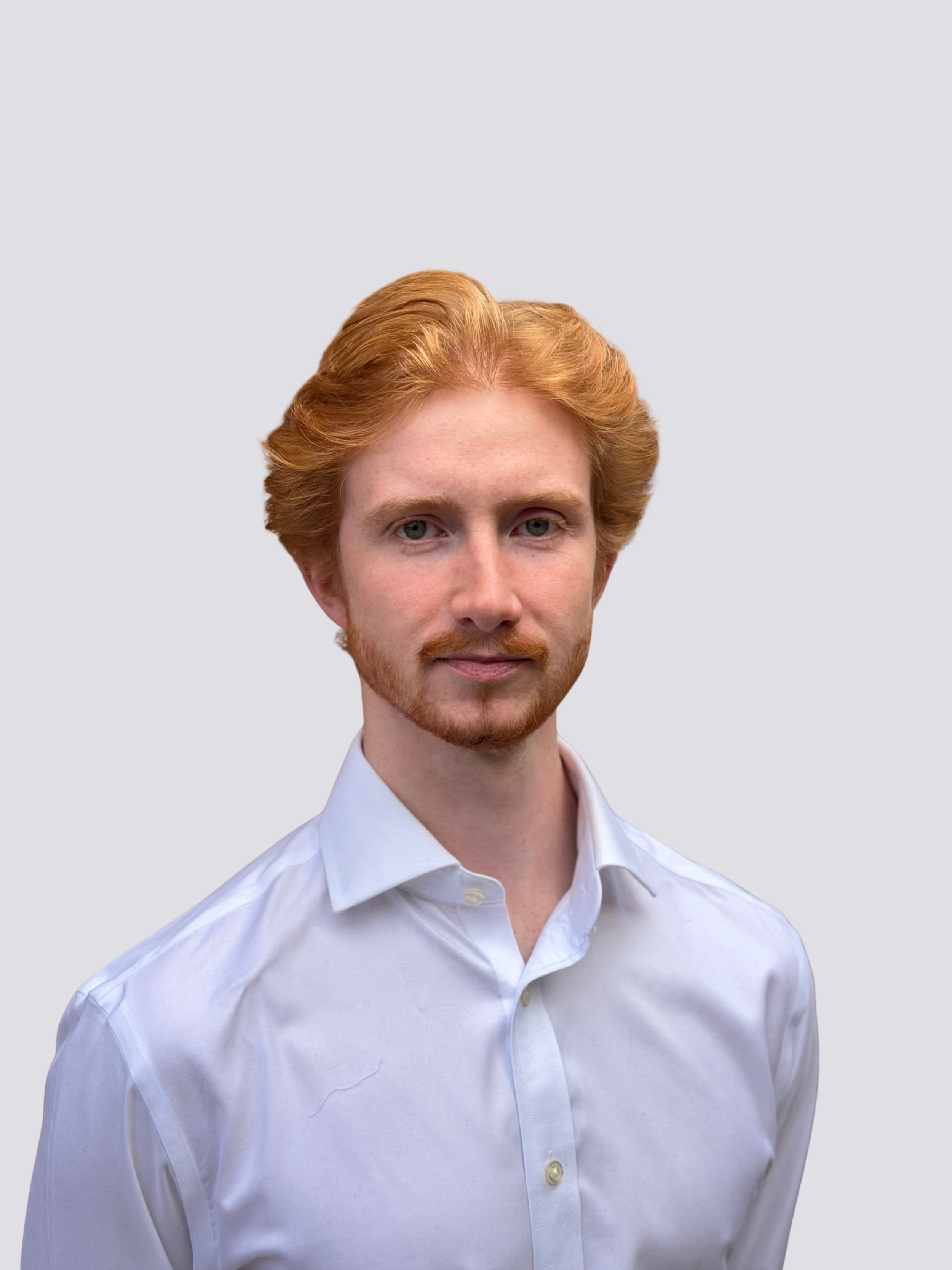 Close-up of a young man with red hair and beard wearing a white dress shirt against a plain light gray background.