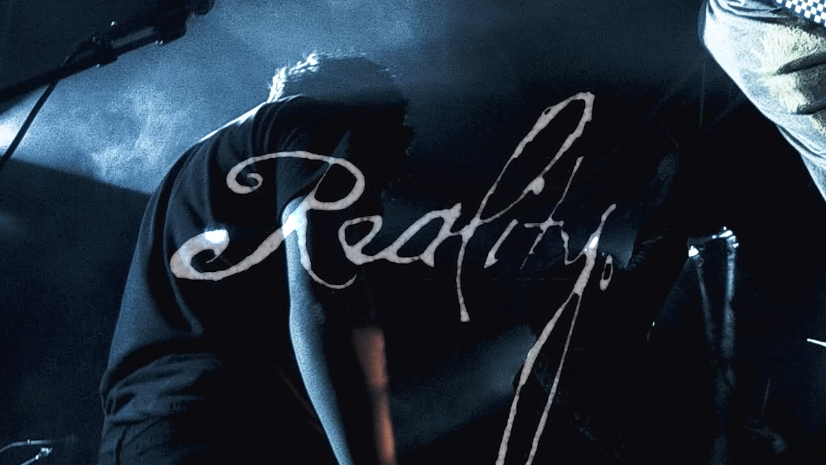 Person sitting with their legs crossed, wearing black pants and a black shirt, with the word 'Reality' written in cursive over the image.