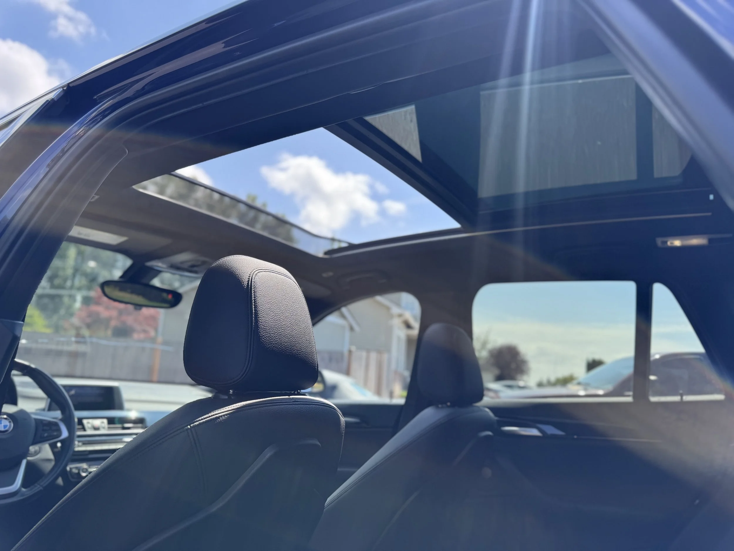 Interior of a modern car with black seats, a panoramic sunroof, and a clear view of the blue sky with clouds outside.