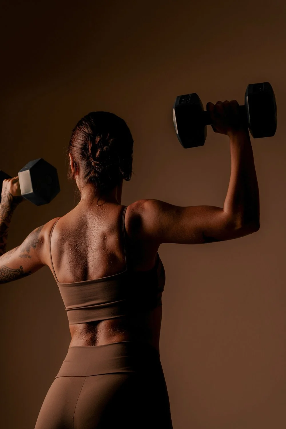 A woman with tattoos lifting dumbbells in a workout studio.