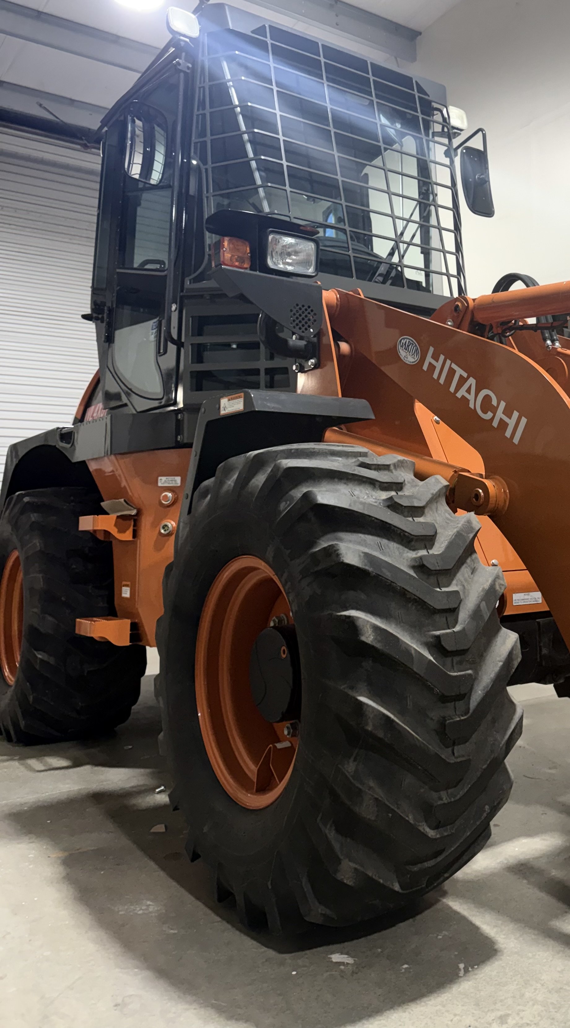 Orange and black Hitachi front-end loader construction vehicle with heavy-duty tires, parked indoors on a concrete floor.