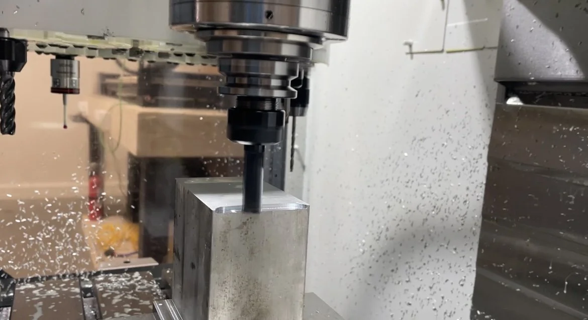 Close-up of a CNC milling machine cutting into a metallic block with metal shavings flying around in a workshop.