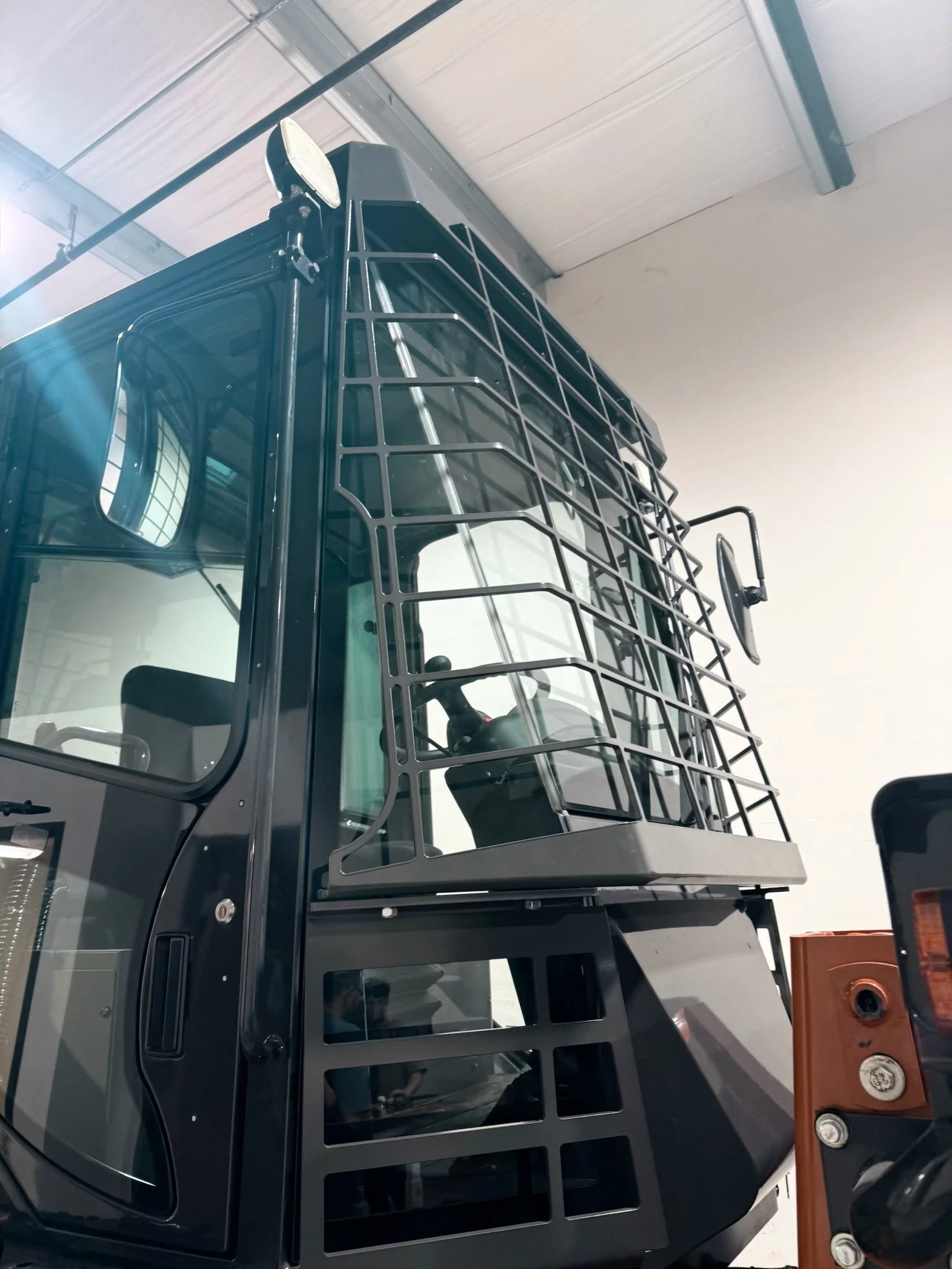 Close-up of a forklift with a protective metal cage around the cab, situated indoors with ceiling and walls visible.