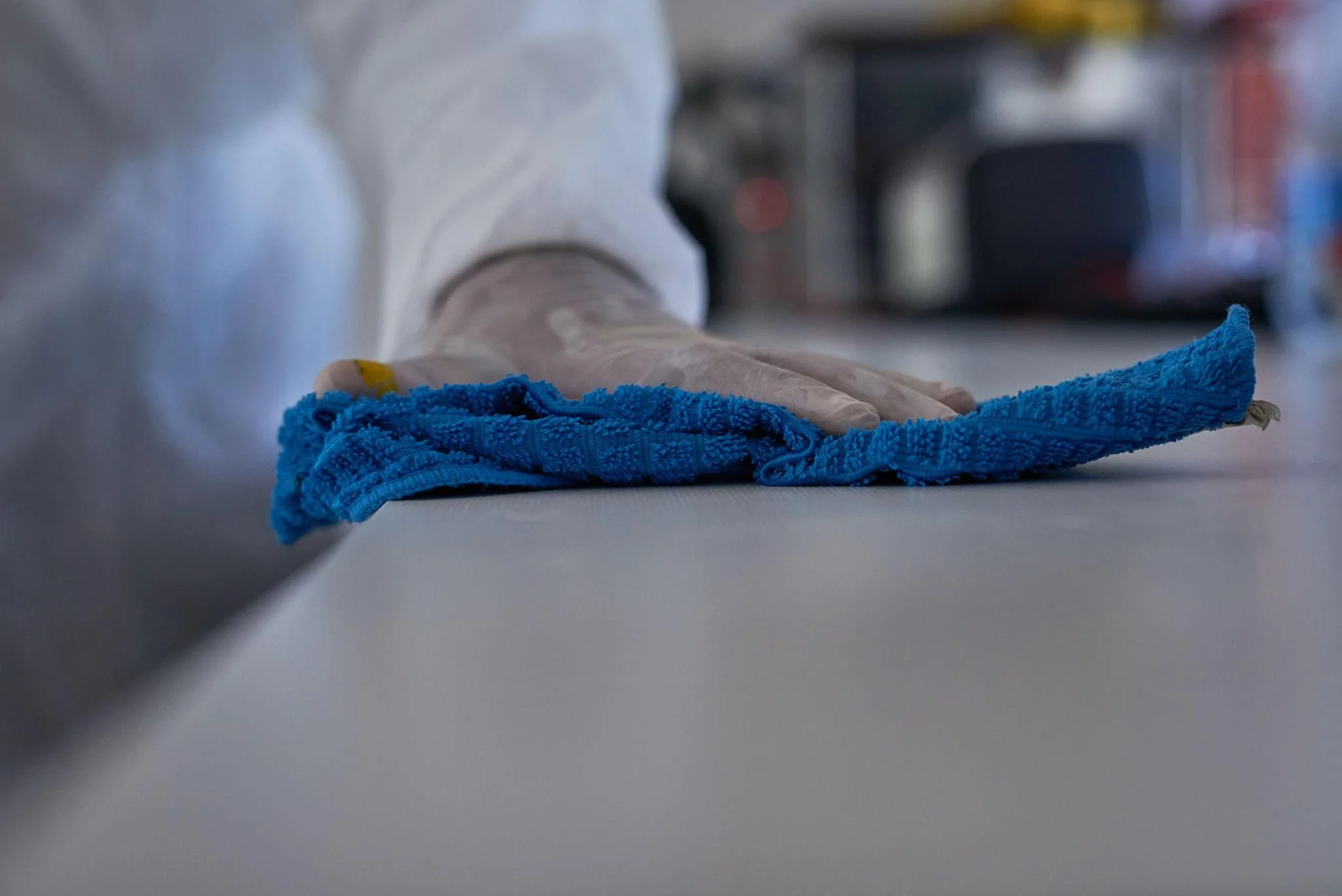 Person wearing gloves cleaning a flat surface with a blue cloth in a kitchen or work environment.