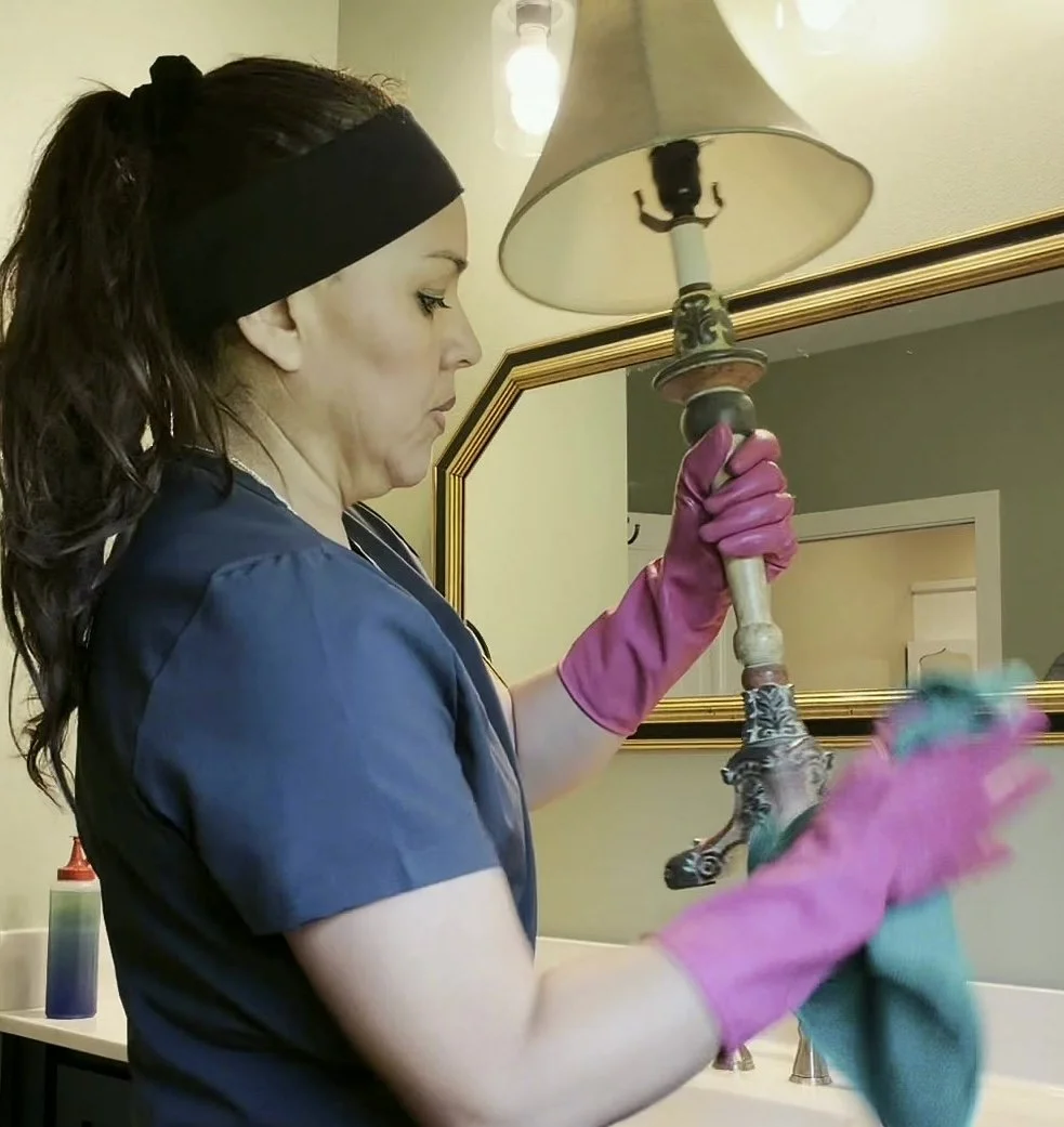 Rosy cleaning a bathroom lamp during a residential cleaning service.