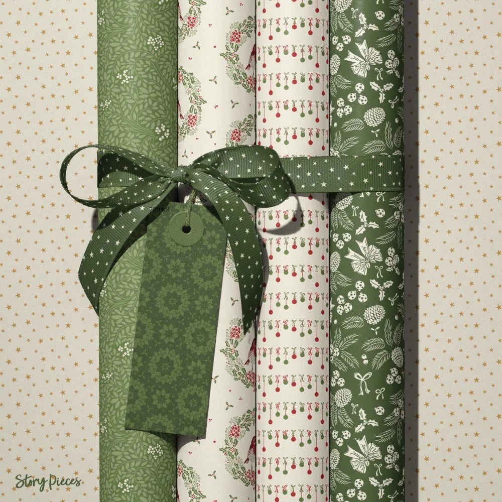 Collection of rolled Christmas wrapping papers in coordinating festive patterns—leafy green, wreaths with birds, ornaments, and woodland motifs—tied with a green star-patterned ribbon and gift tag, set against a soft starry background.