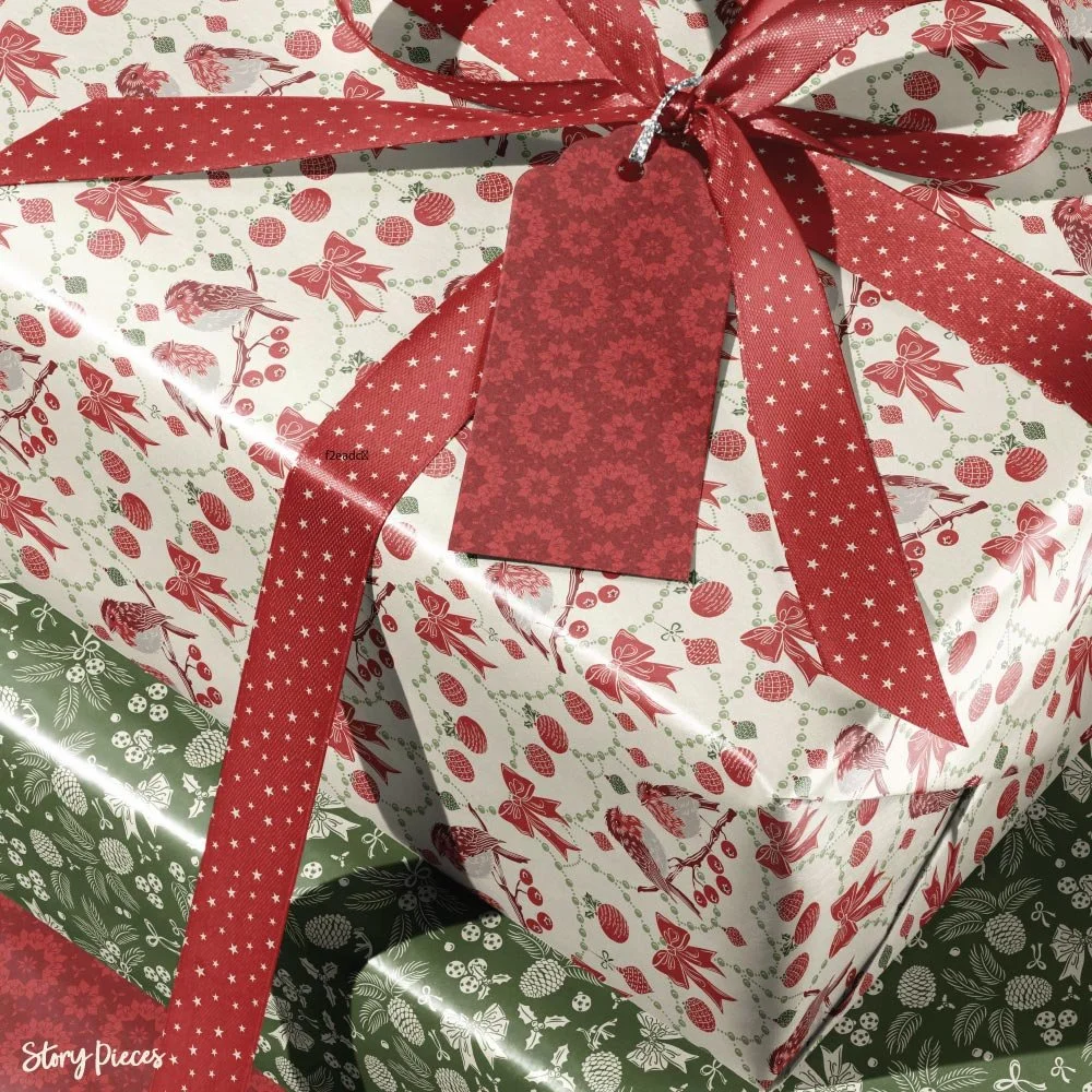 Close-up of a wrapped Christmas gift in festive paper featuring birds, bows, and ornaments, tied with a red ribbon with white stars and finished with a coordinating red gift tag, layered over green woodland-patterned wrapping paper.
