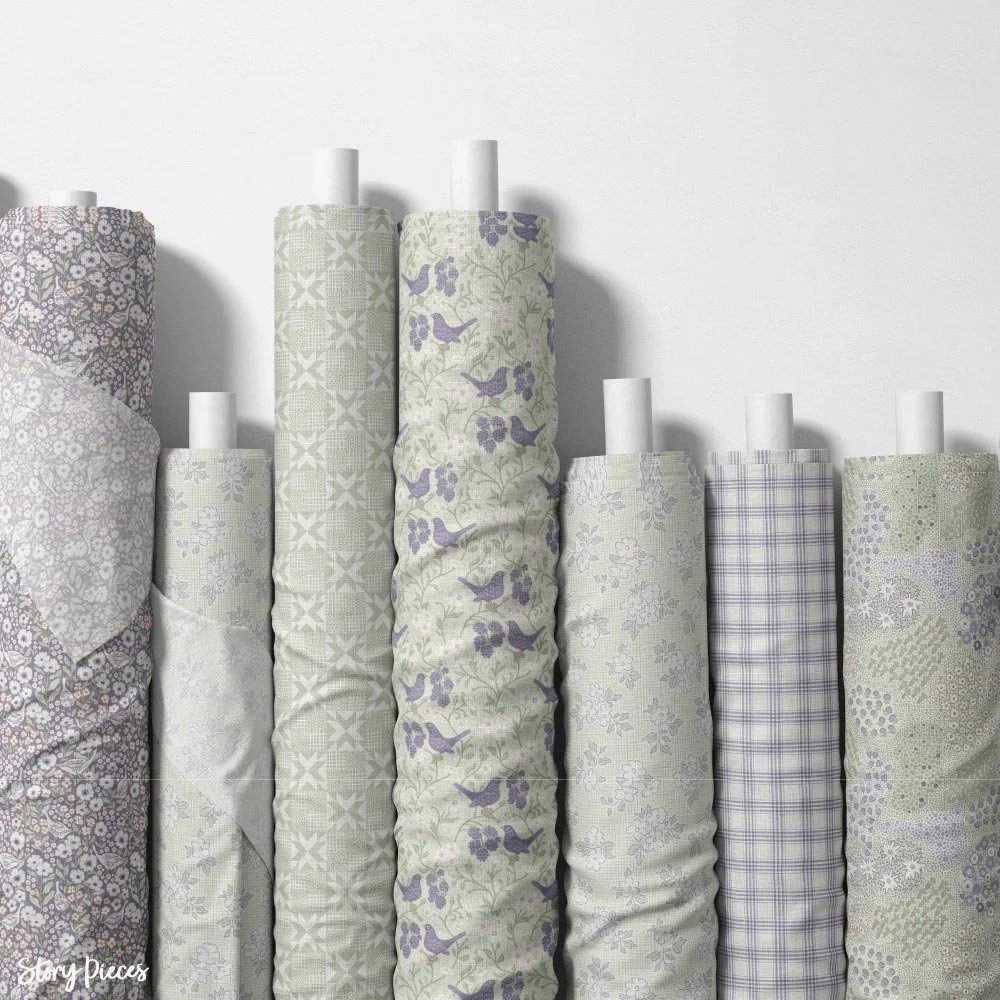 Fabric rolls with vintage-inspired floral and bird patterns in soft green and lavender tones, quilting textile collection display.