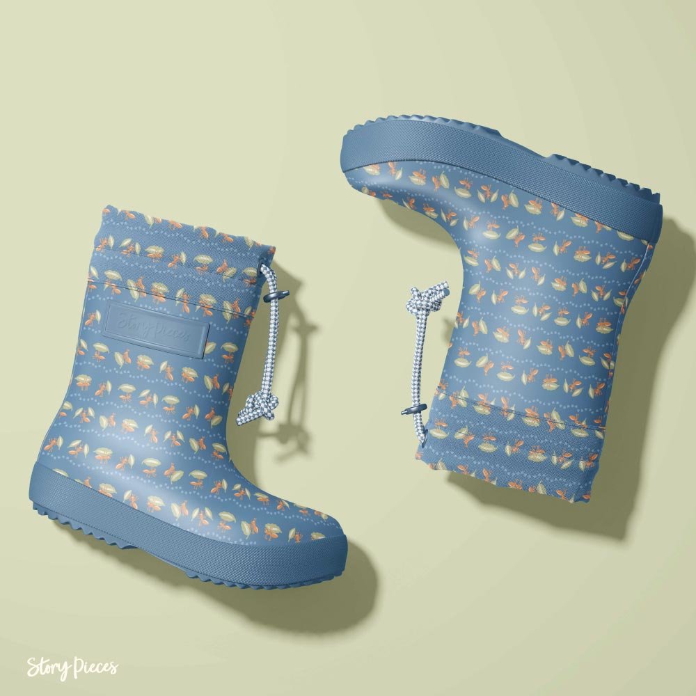 Pair of children’s rubber boots in a soft blue tone, featuring a small-scale pattern of insects and nature motifs, shown from two angles against a muted green background.