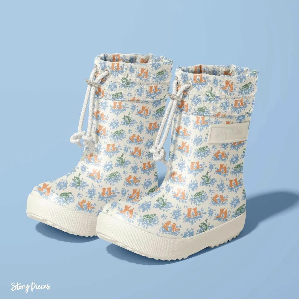 Pair of children’s rubber boots featuring a playful pattern of frogs, puddles, and orange gumboots on a light background, set against a soft blue backdrop.