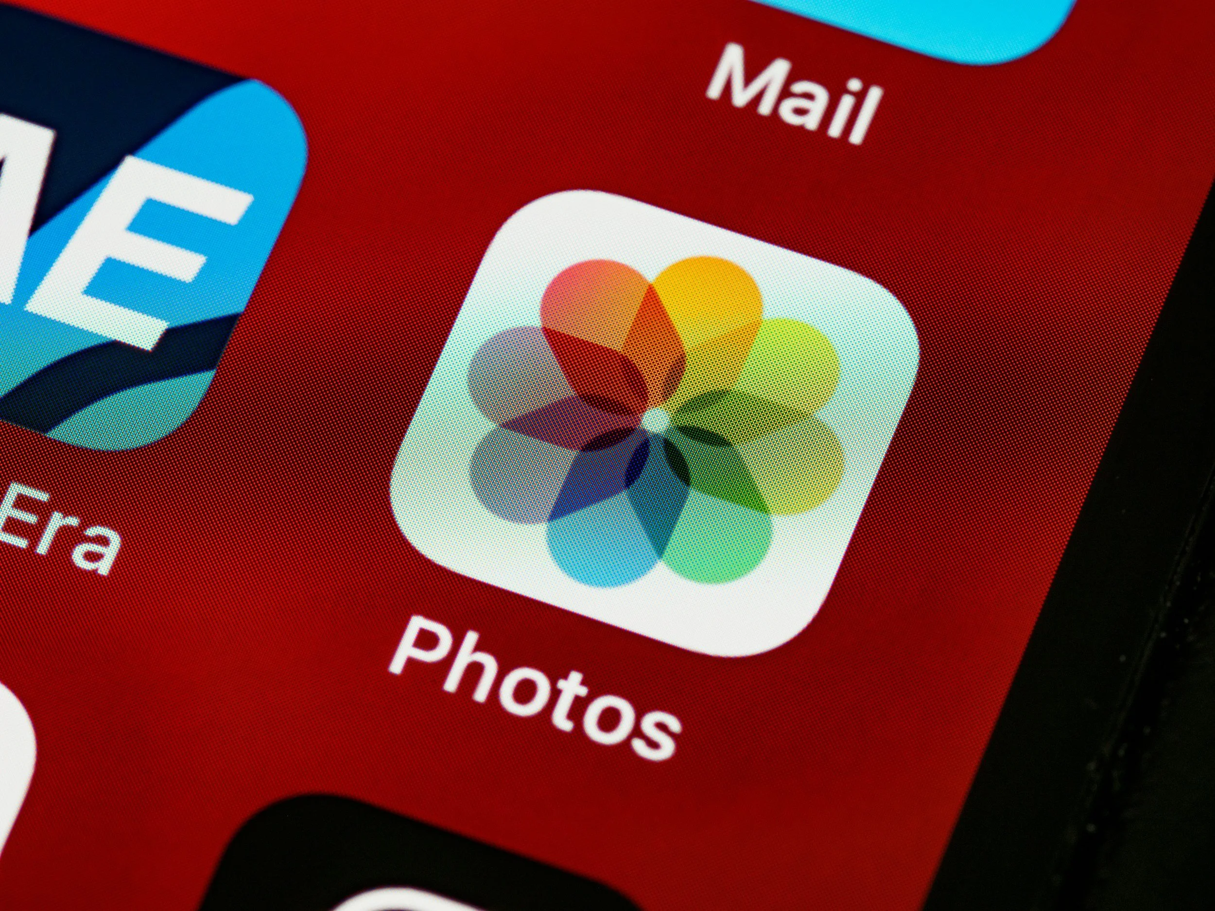Extreme close-up of the Apple Photos and Mail app icons on an iPhone home screen with a red background.