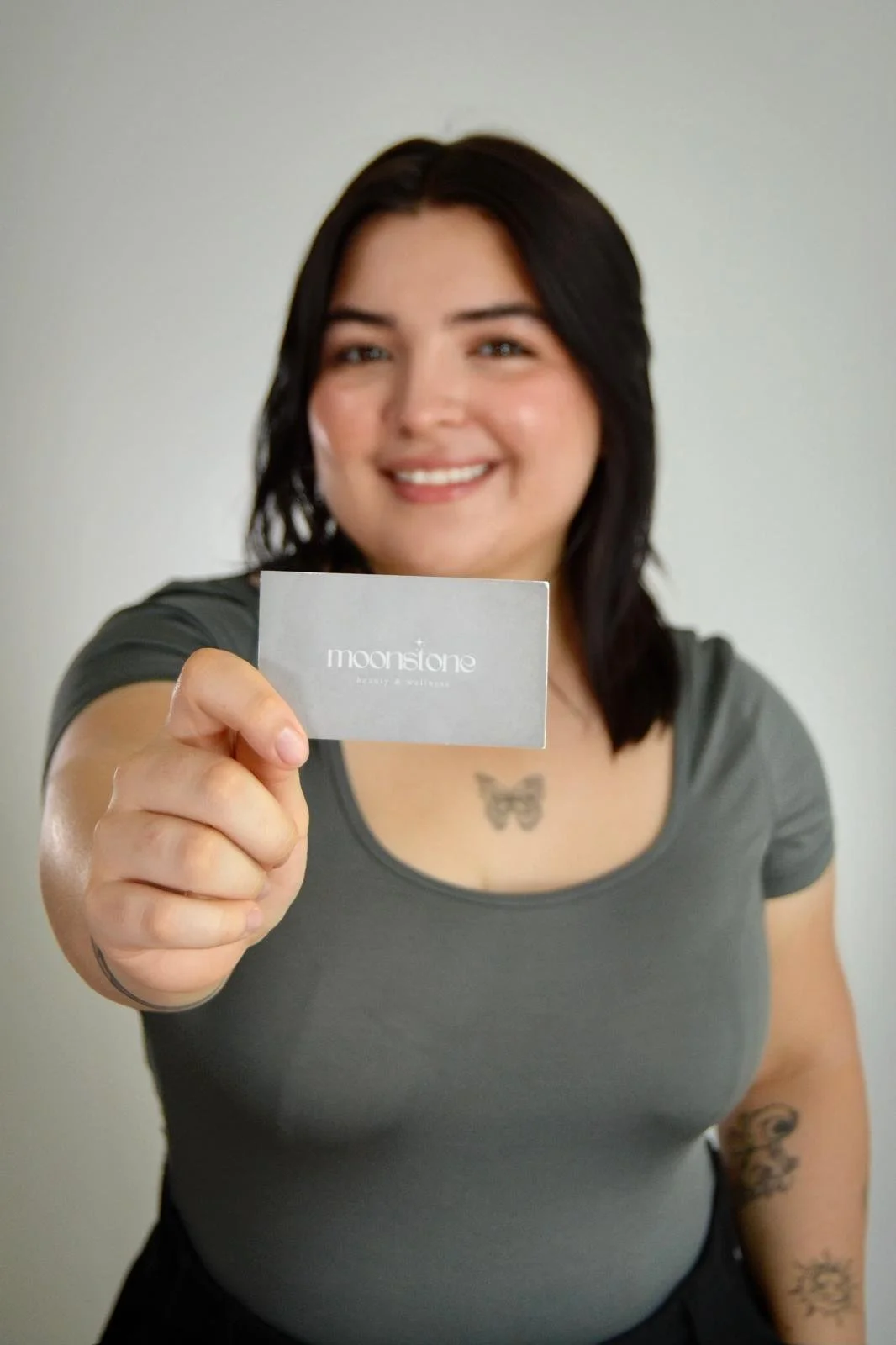 Smiling woman holding a business card that says 'moonstone beauty & wellness.'