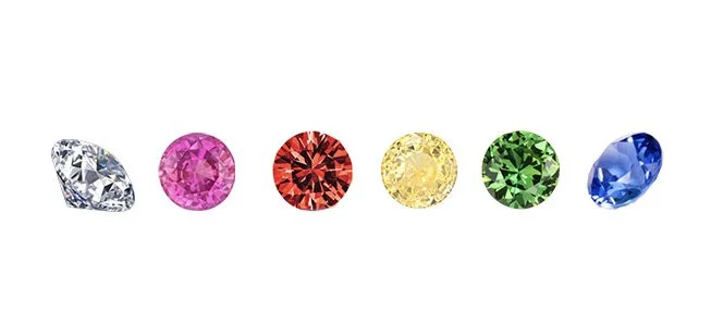 Six colorful gemstones arranged in a row, from clear to blue, including pink, red, yellow, green, and blue stones.