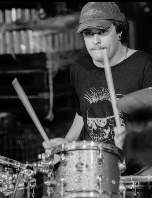 A young person wearing a baseball cap and a T-shirt playing drums.