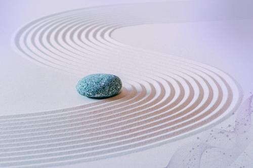A single gray stone on a white Zen garden with raked sand and curved lines.