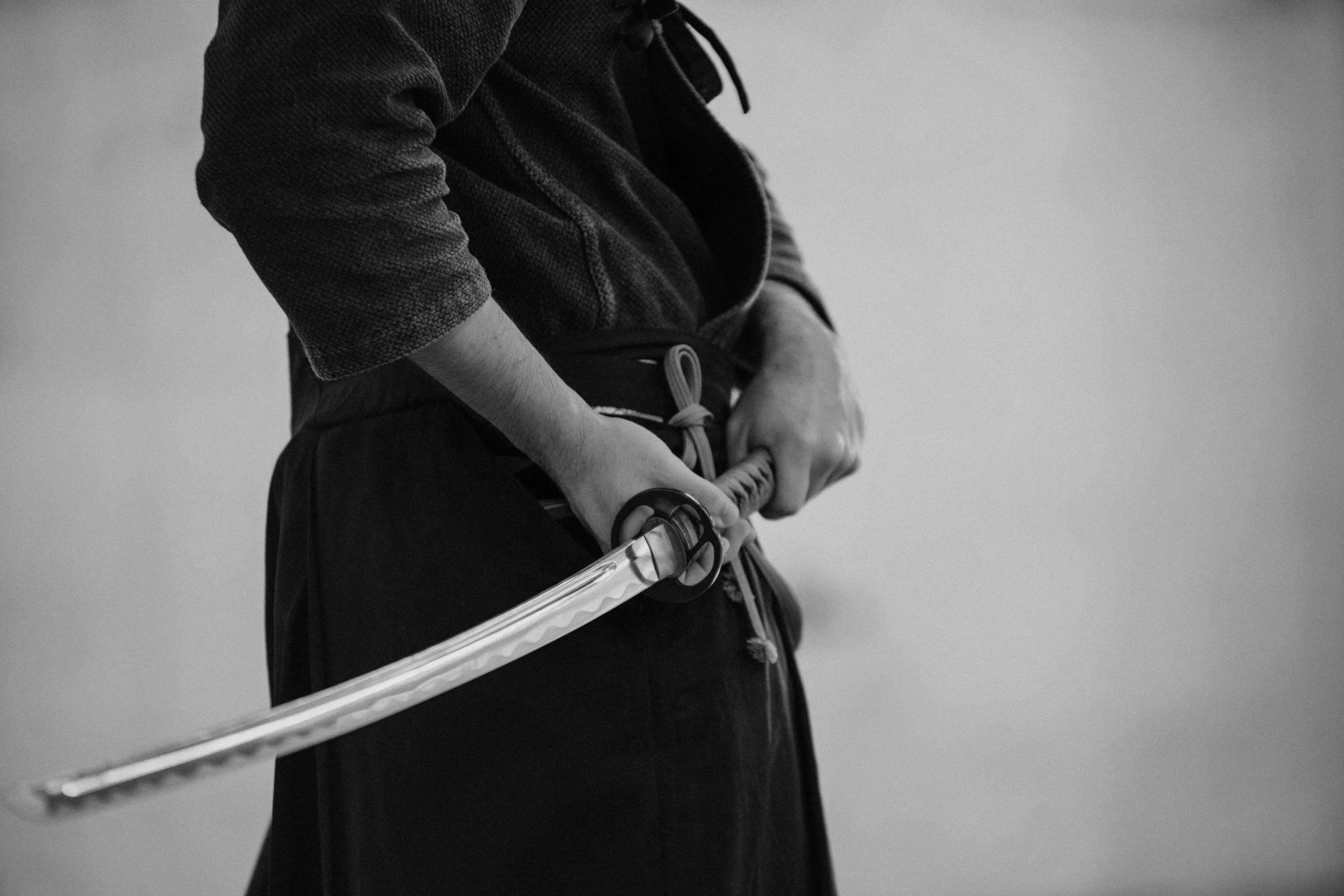 A person dressed in dark clothing is holding a sword with both hands, positioned in front of their body.