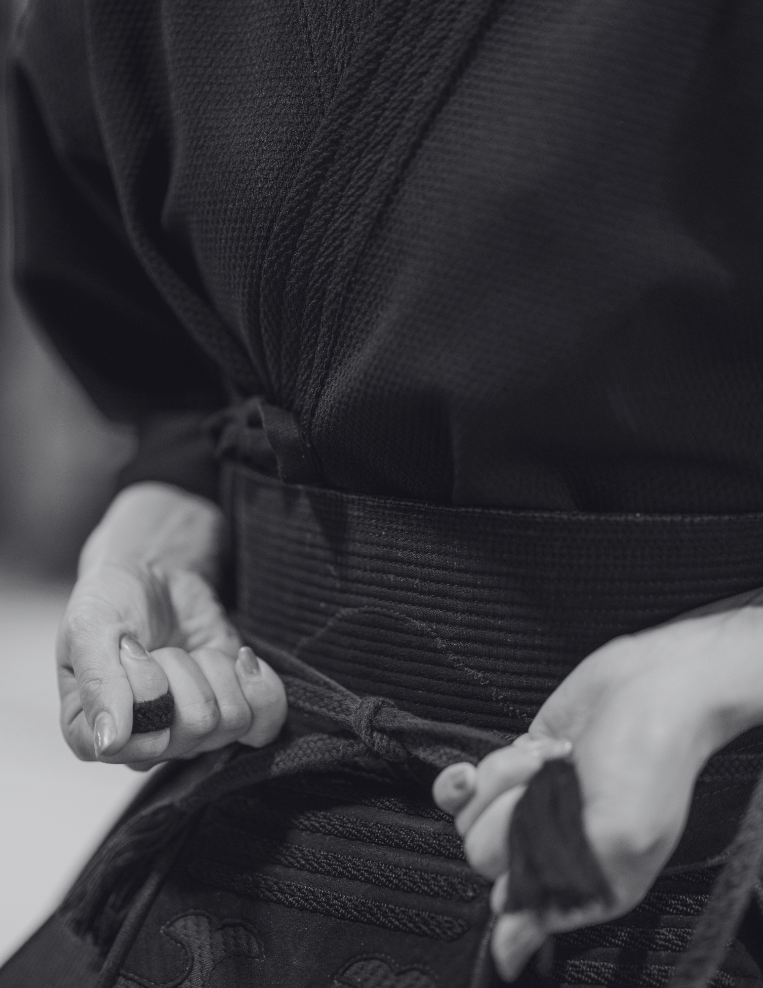 Close-up black and white photo of a person securing an obi to their martial arts gi.