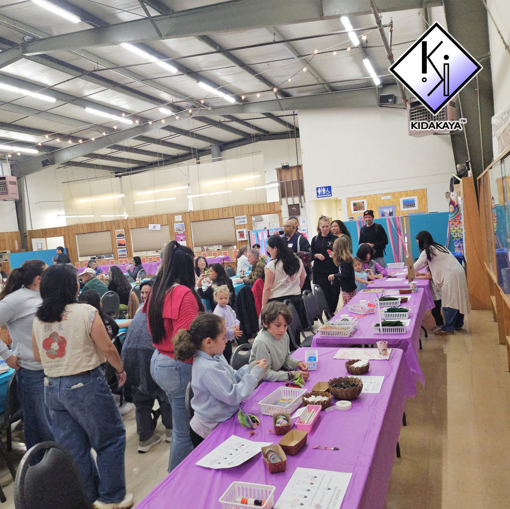 People gathered around tables with arts and crafts supplies inside a large indoor space with high ceiling and industrial lighting.