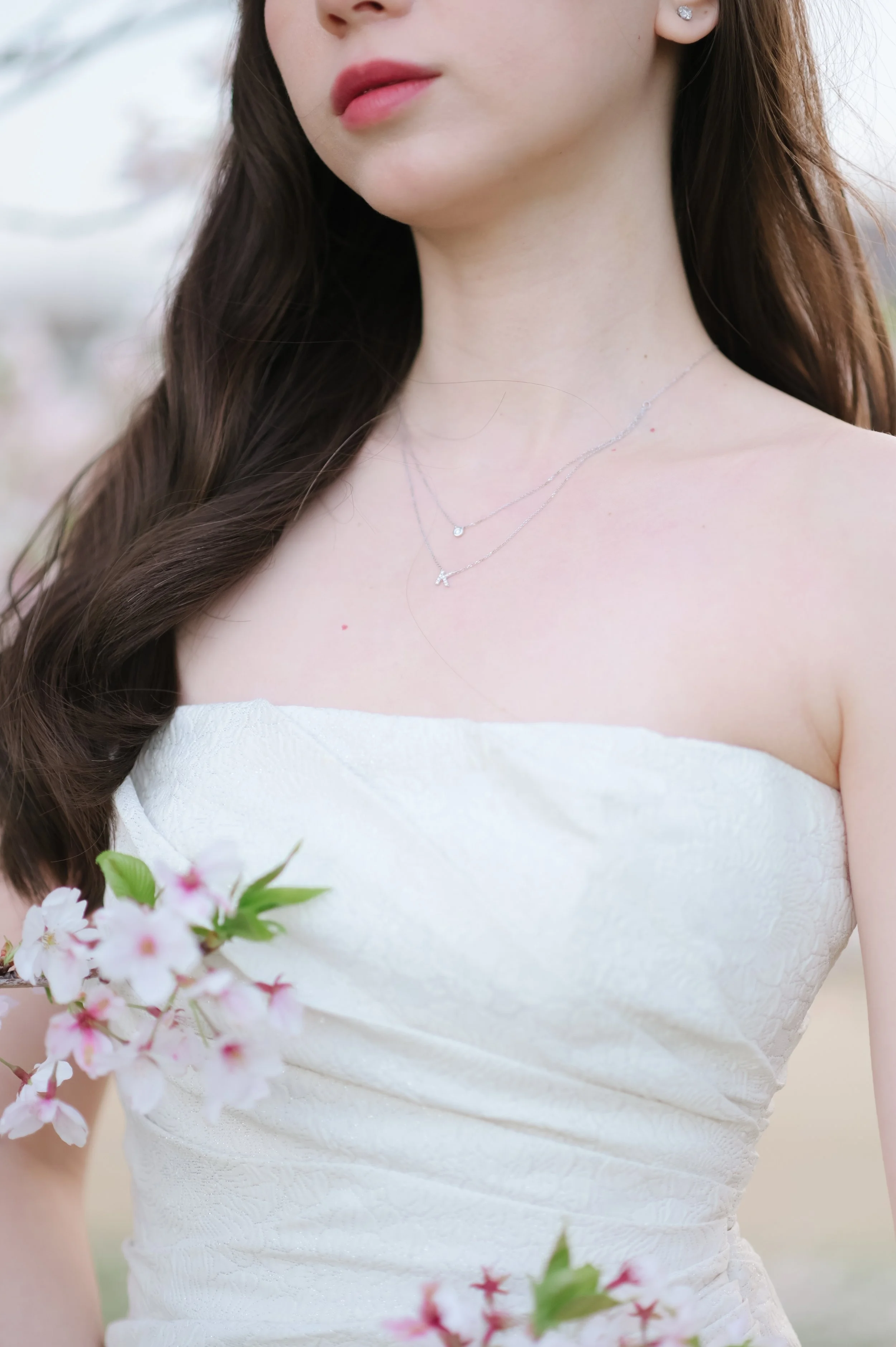 白いドレスを着た女性の胸元とネックレス、花飾りを持つ。