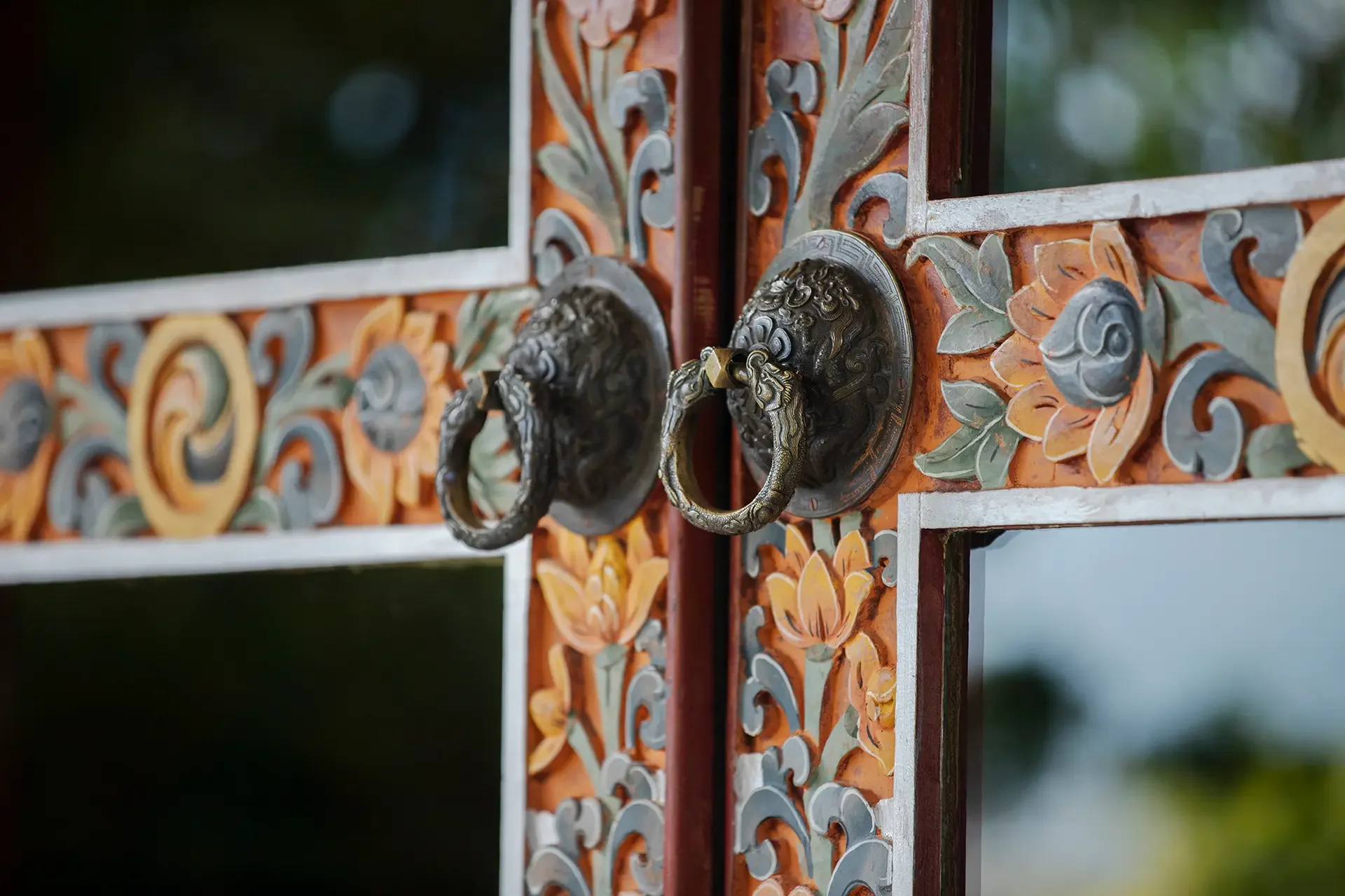 Close-up of an ornate metal gate with intricate leaf and swirl designs, featuring two lion head door knockers with ring handles.