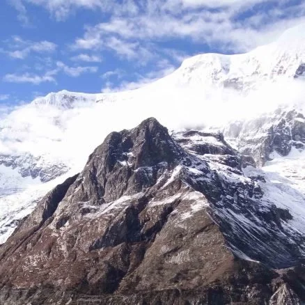 Snow-capped mountain surrounded by blue sky and clouds.