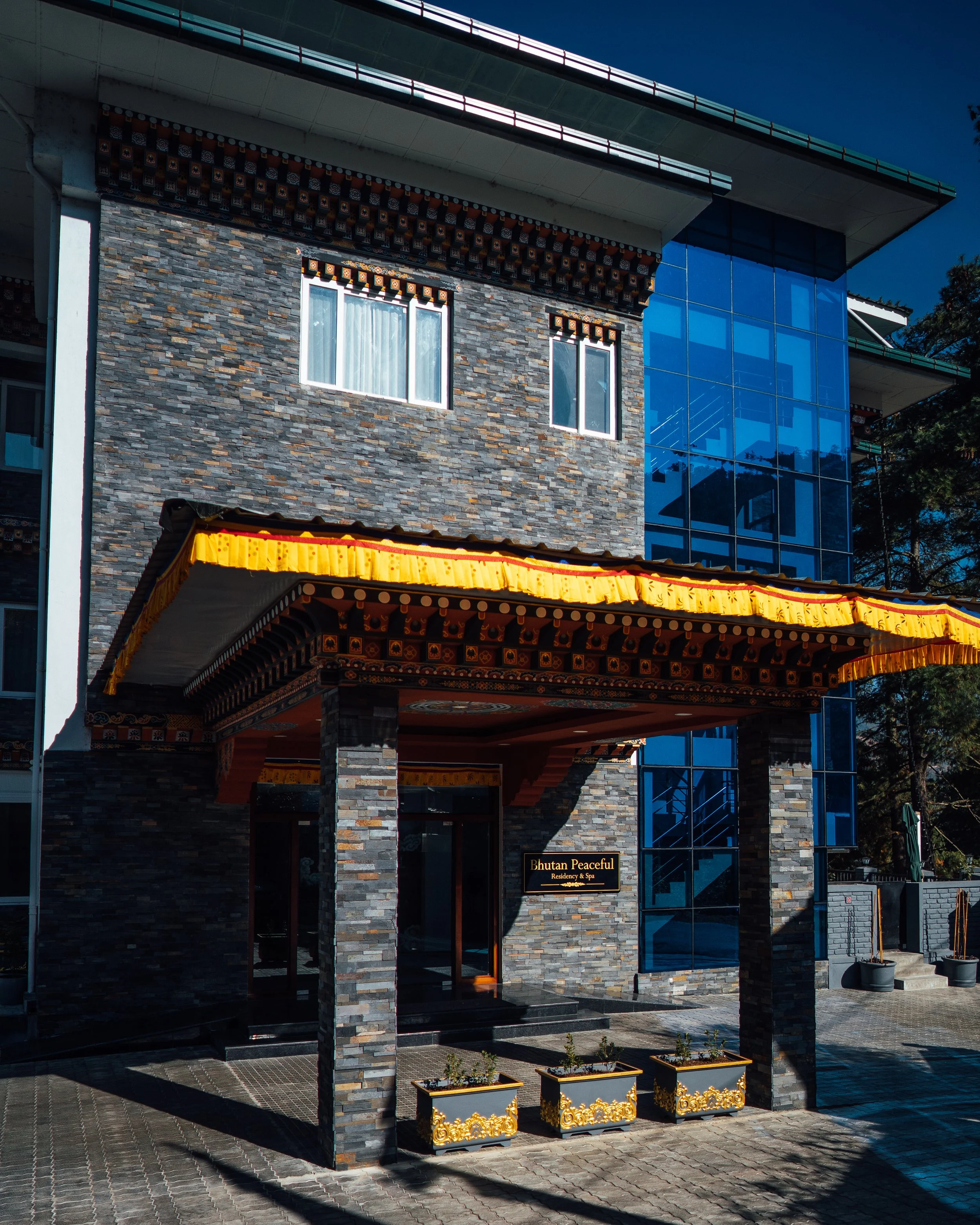 Exterior of Bhutan Peaceful Residence & Spa, featuring a modern building with stone and glass facade, decorative elements, and potted plants at the entrance.