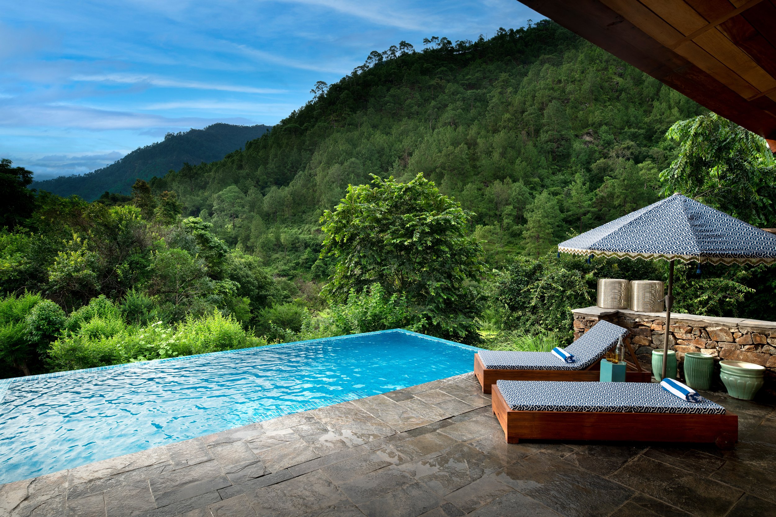 Swimming pool with mountain and forest view, poolside lounge chairs, terrace umbrella, and hillside landscape.