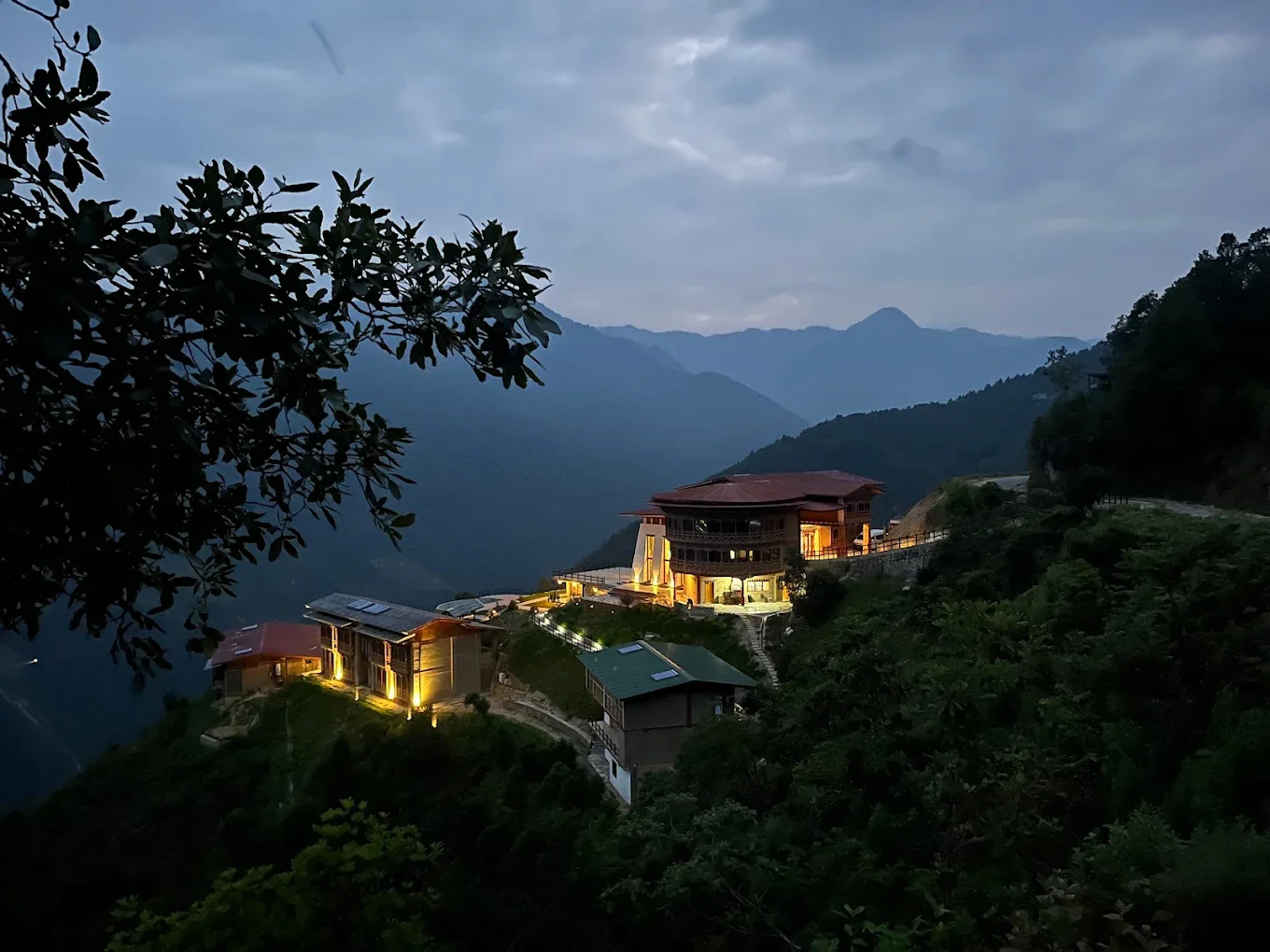 Mountains at dusk with a house on a hillside illuminated by lights.