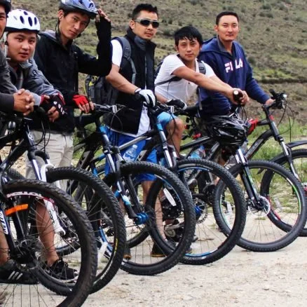 Five young men standing with bicycles outdoors, with a hilly landscape in the background.