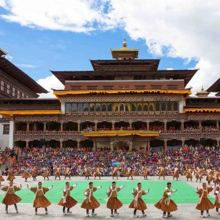 A traditional cultural dance performance in front of a multi-tiered pagoda-style building with a large audience watching.