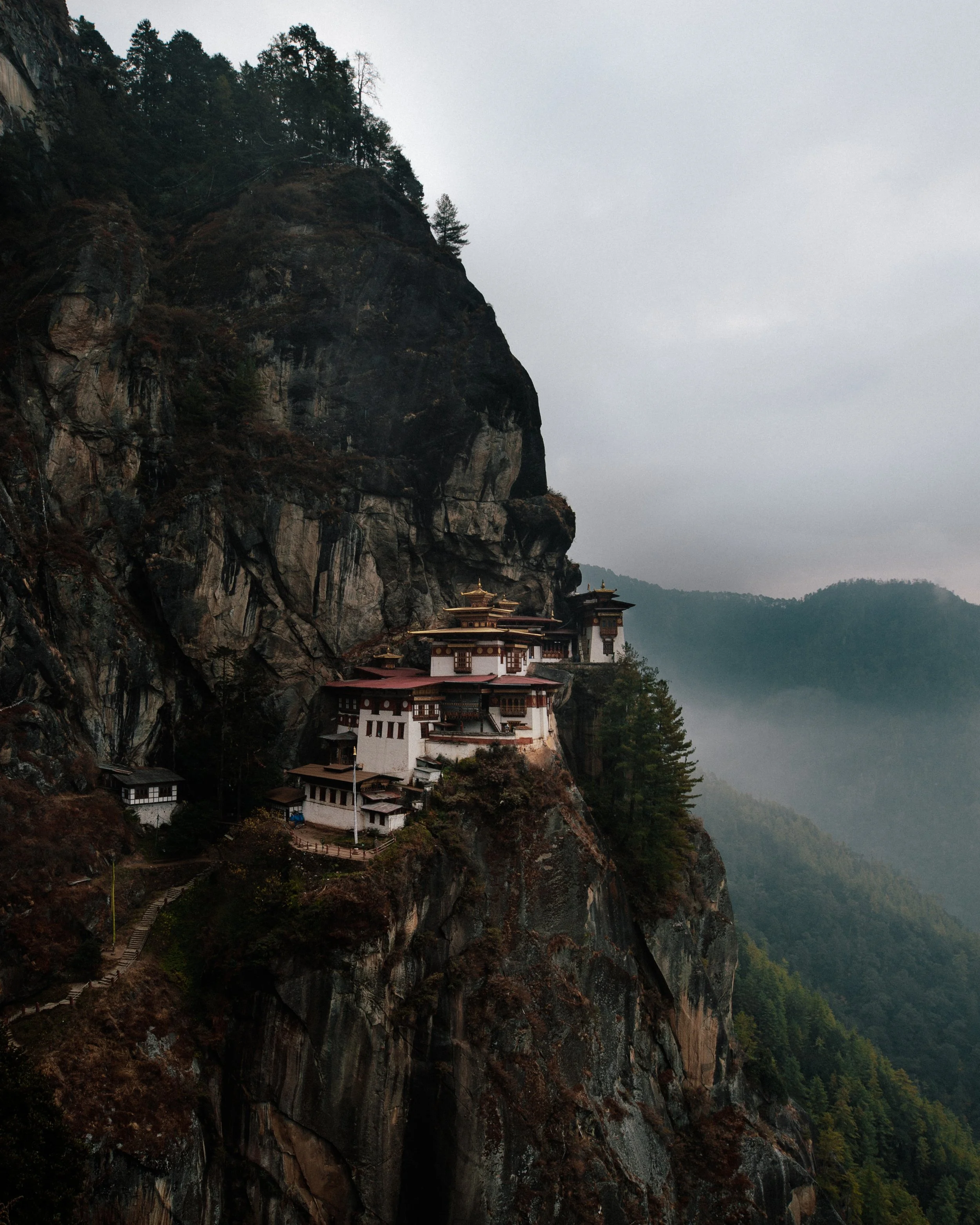 A temple on a mountain cliff with trees and a foggy landscape in the background.