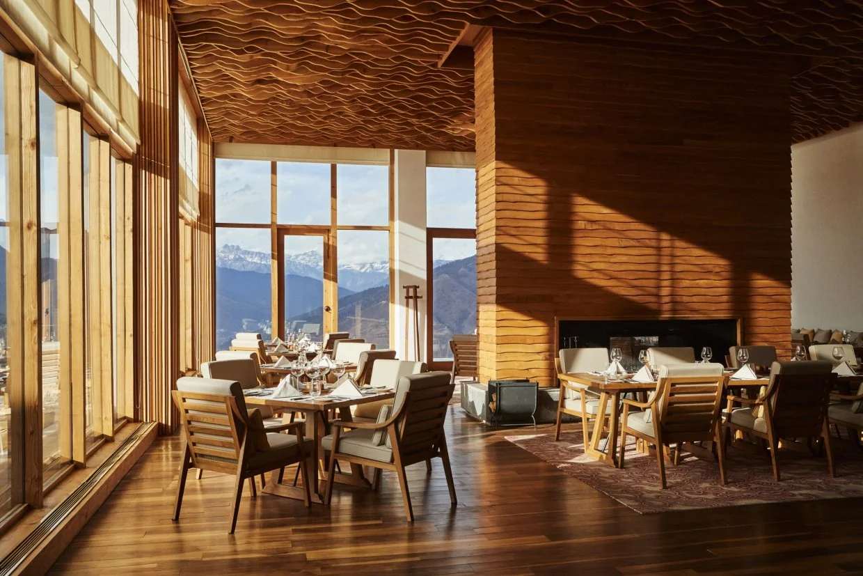 Elegant restaurant interior with wooden furniture, large windows, mountain views, and fireplace.