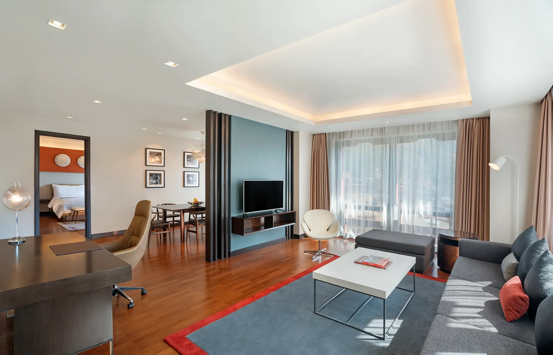 Modern living room with large window, gray and white furniture, wooden flooring, and decorative lighting.