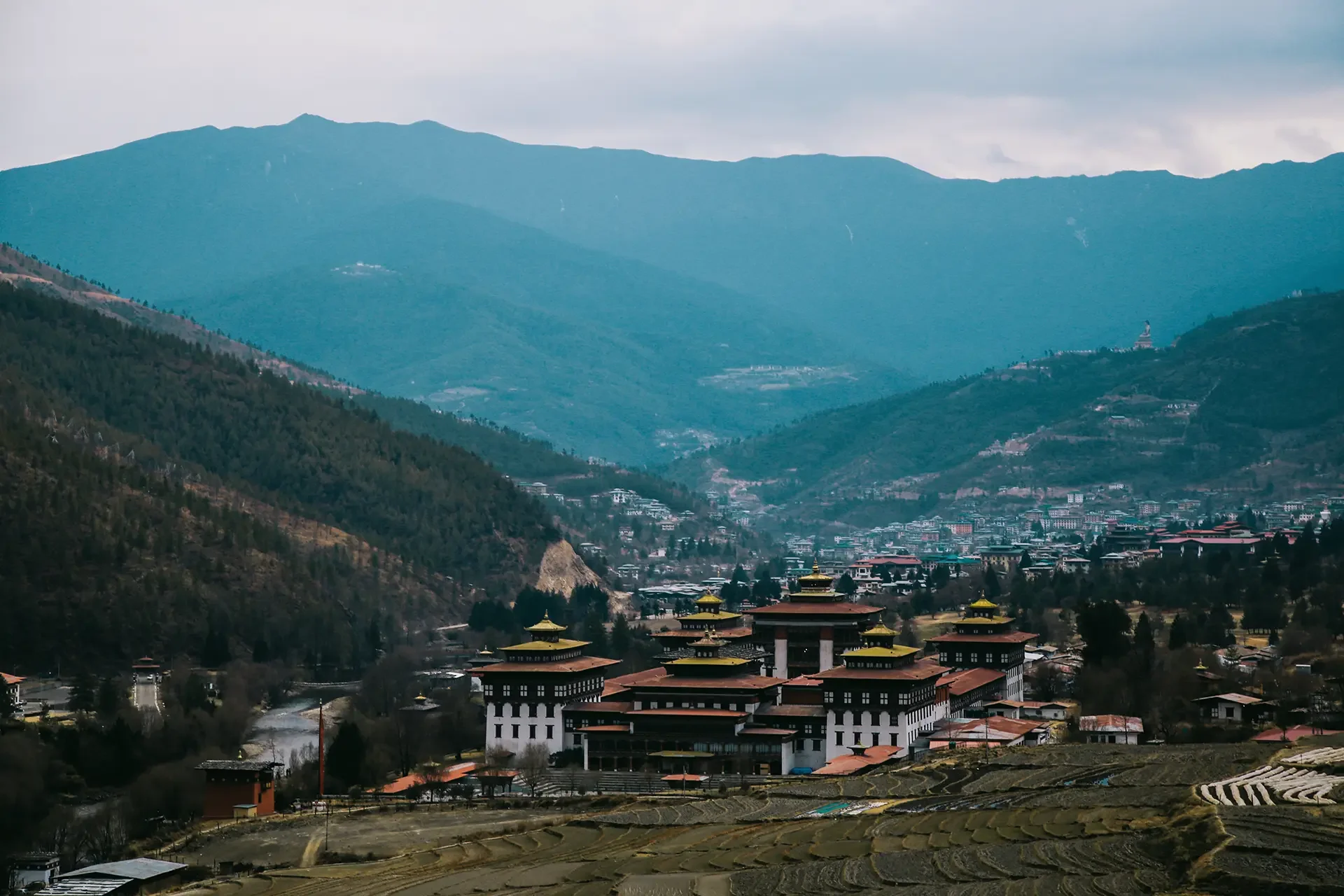 A scenic view of a valley surrounded by mountains with a small town at the base and traditional buildings with golden roofs in the foreground.