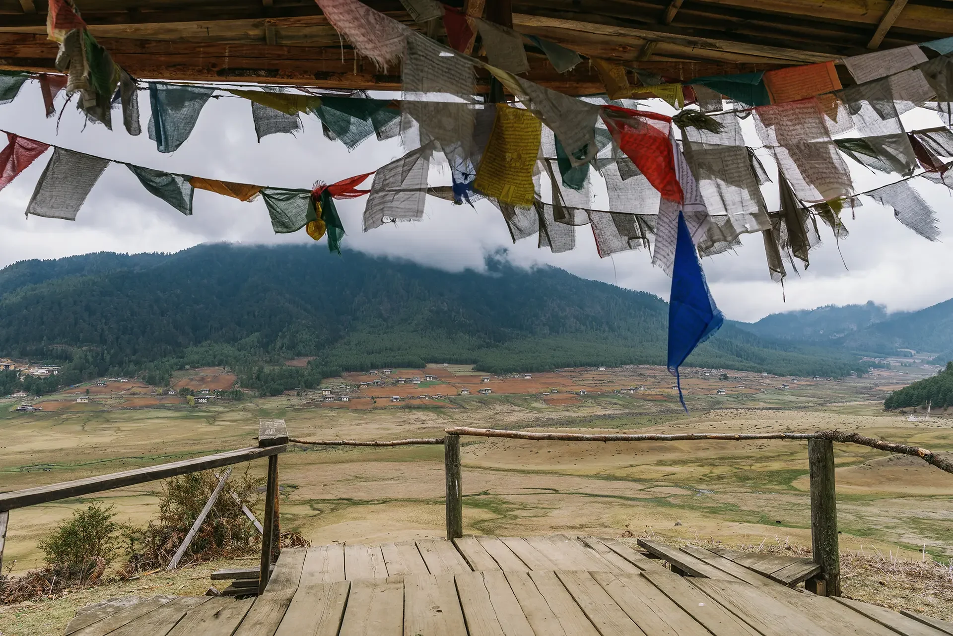 Mountains in the background with prayer flags hanging in the foreground and an empty wooden deck.