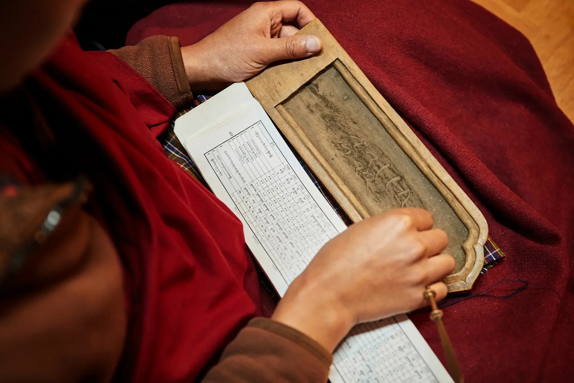Person holding a wooden frame with a sheet of paper containing a chart or schedule inside