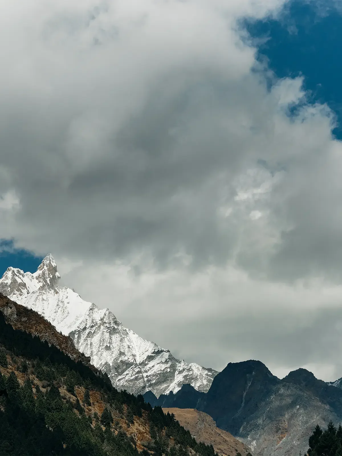 Snow-capped mountains under a cloudy sky with some blue sky peeking through.