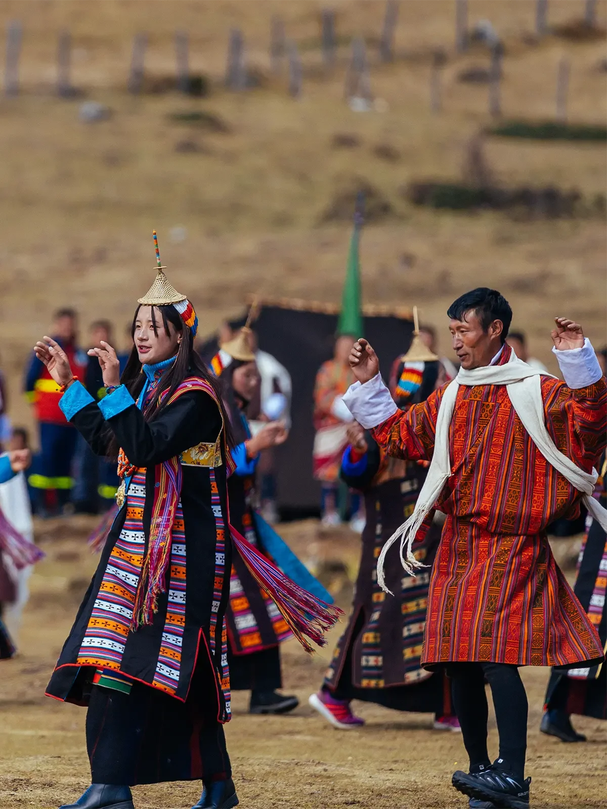 People dancing outdoors in traditional Andean clothing, with colorful woven garments and hats, during a cultural celebration or festival.