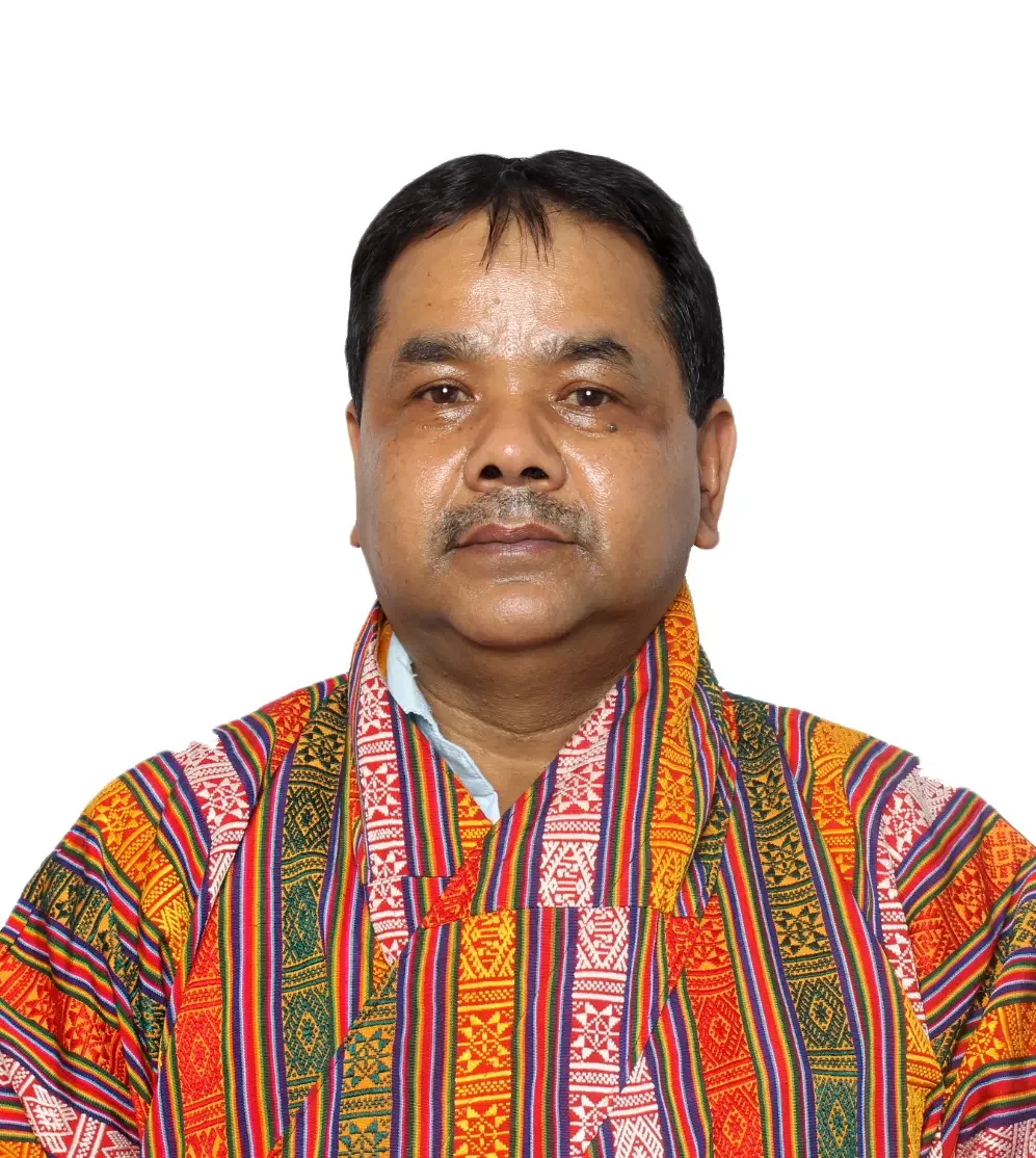 A man wearing a colorful, patterned shirt or robe, standing against a plain white background.