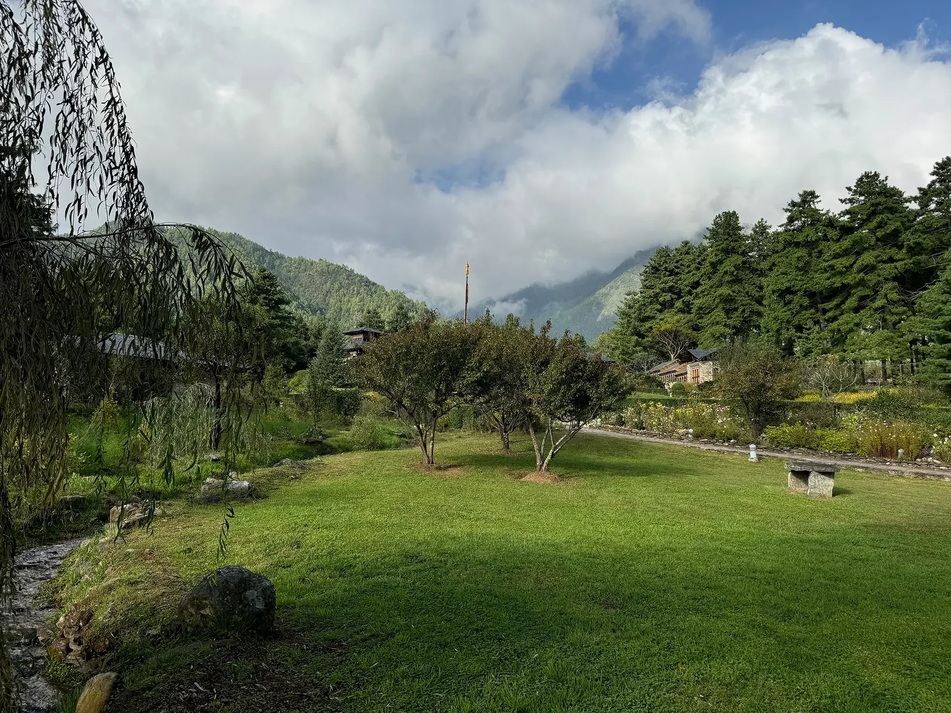 A lush green landscape with trees and grass, mountains in the background, and a partly cloudy sky overhead.