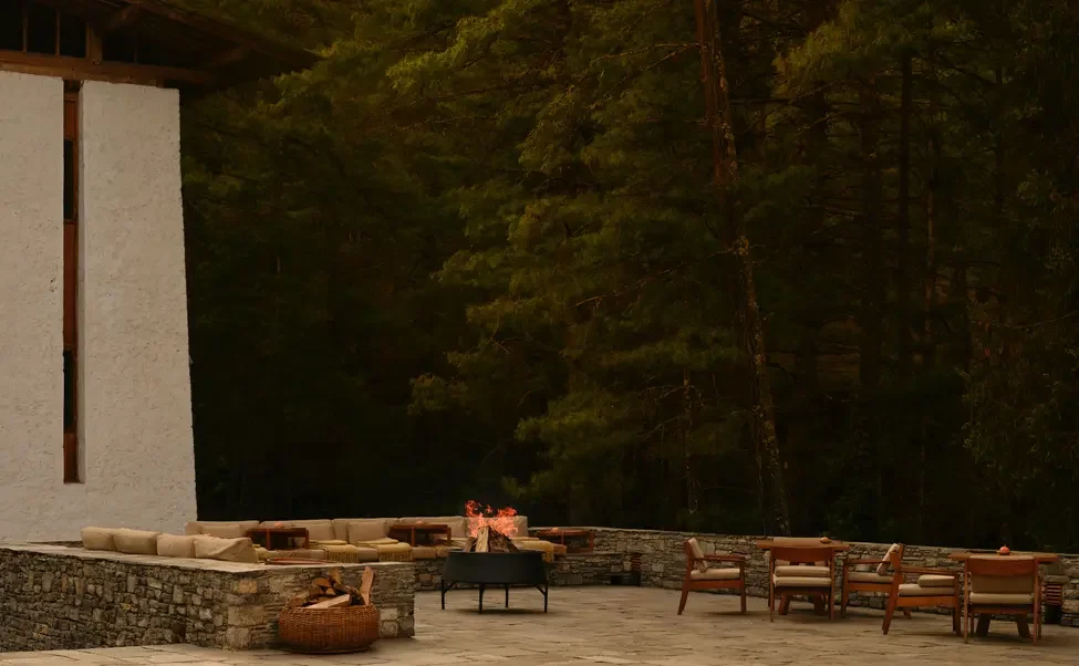 Outdoor patio area with seating, firepit, and a wooded forest background at dusk.