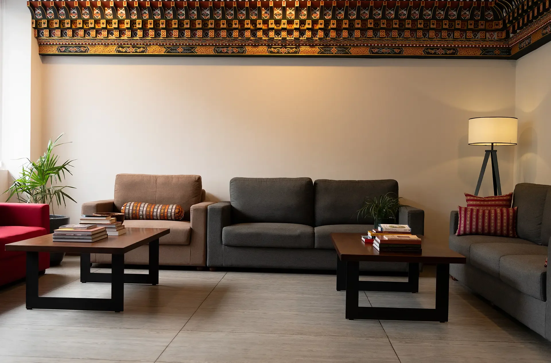 Living room with various sofas, coffee tables, plants, a floor lamp, and decorative pillows, with a colorful patterned ceiling design.