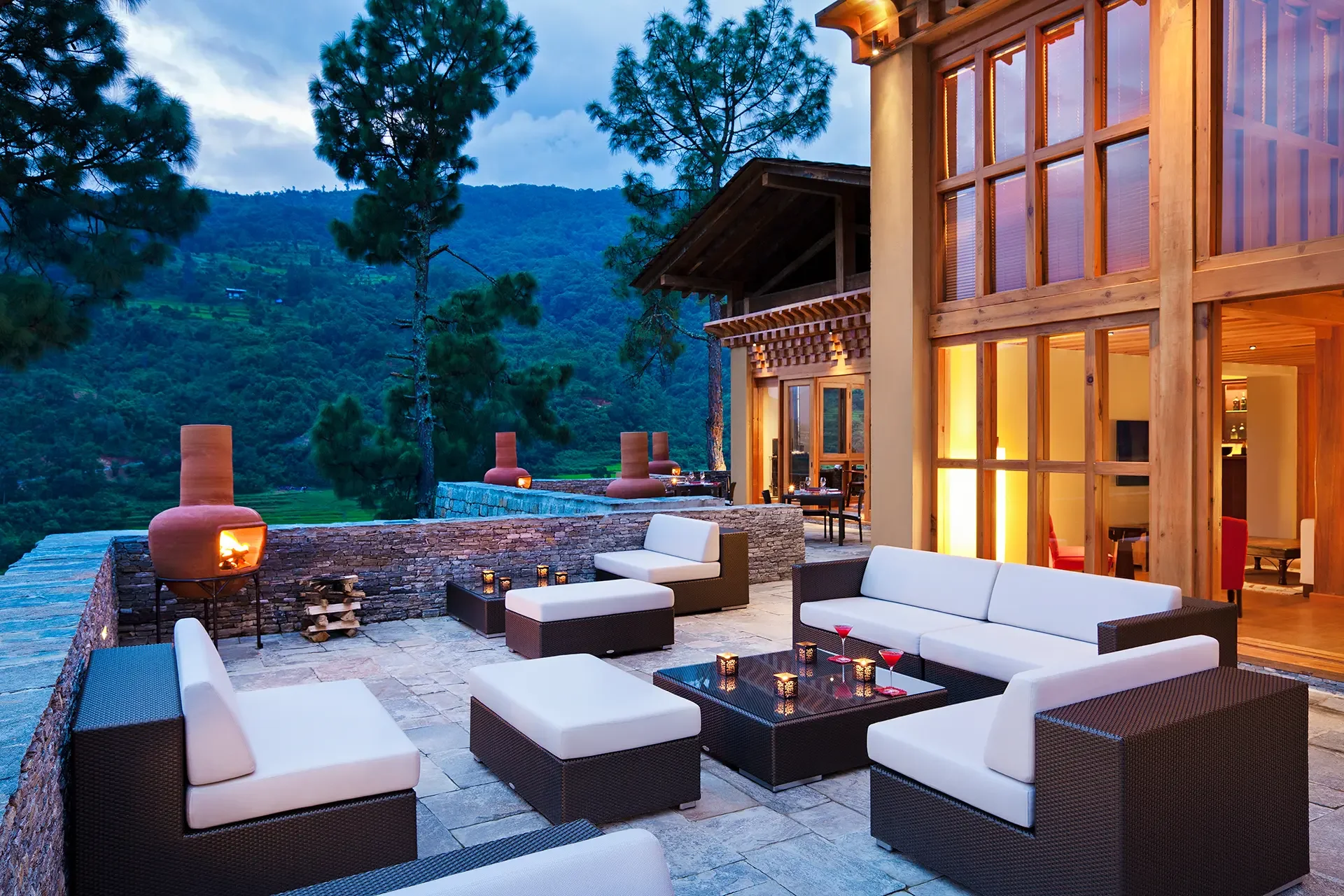 Outdoor luxury patio at dusk with modern furniture, fire pits, and a scenic mountain view in the background.