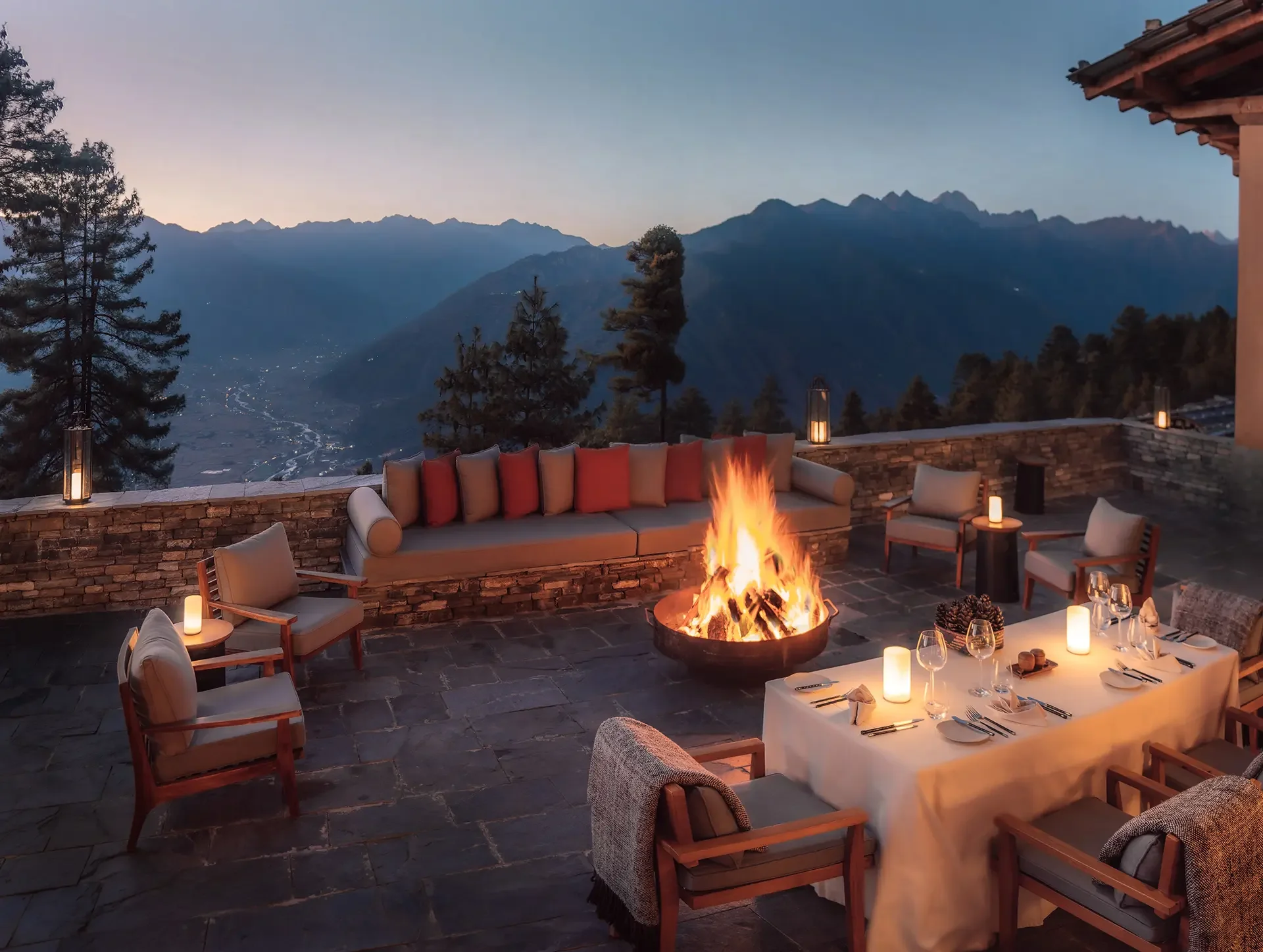 Outdoor dining area at sunset with mountains in the background, a fire pit, and tables set with dinnerware.