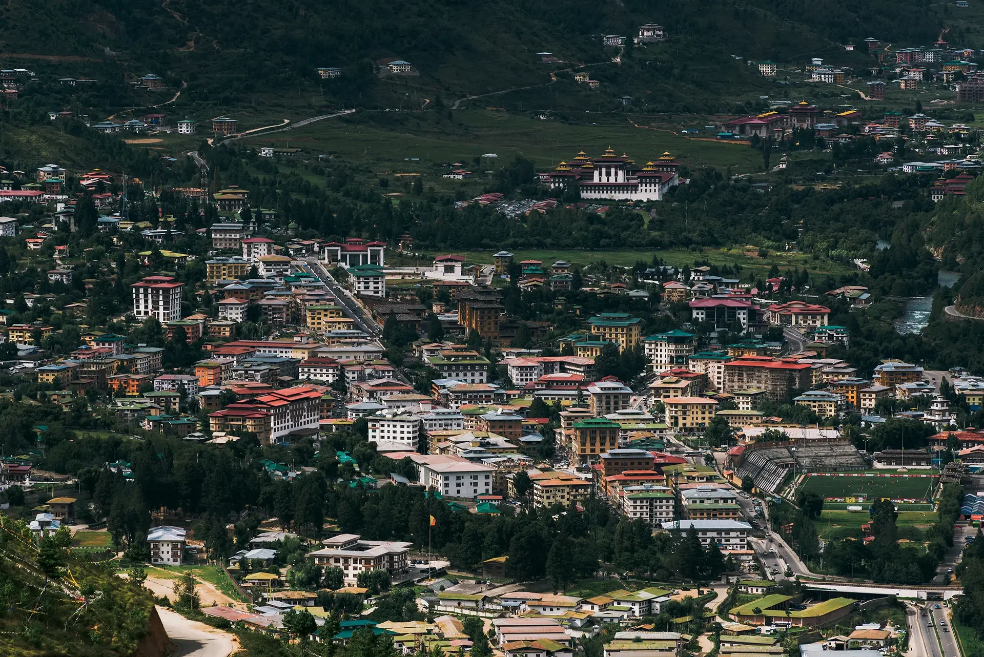 A panoramic view of a town nestled in a lush, green mountainous region with diverse buildings, roads, and a river flowing through the landscape.