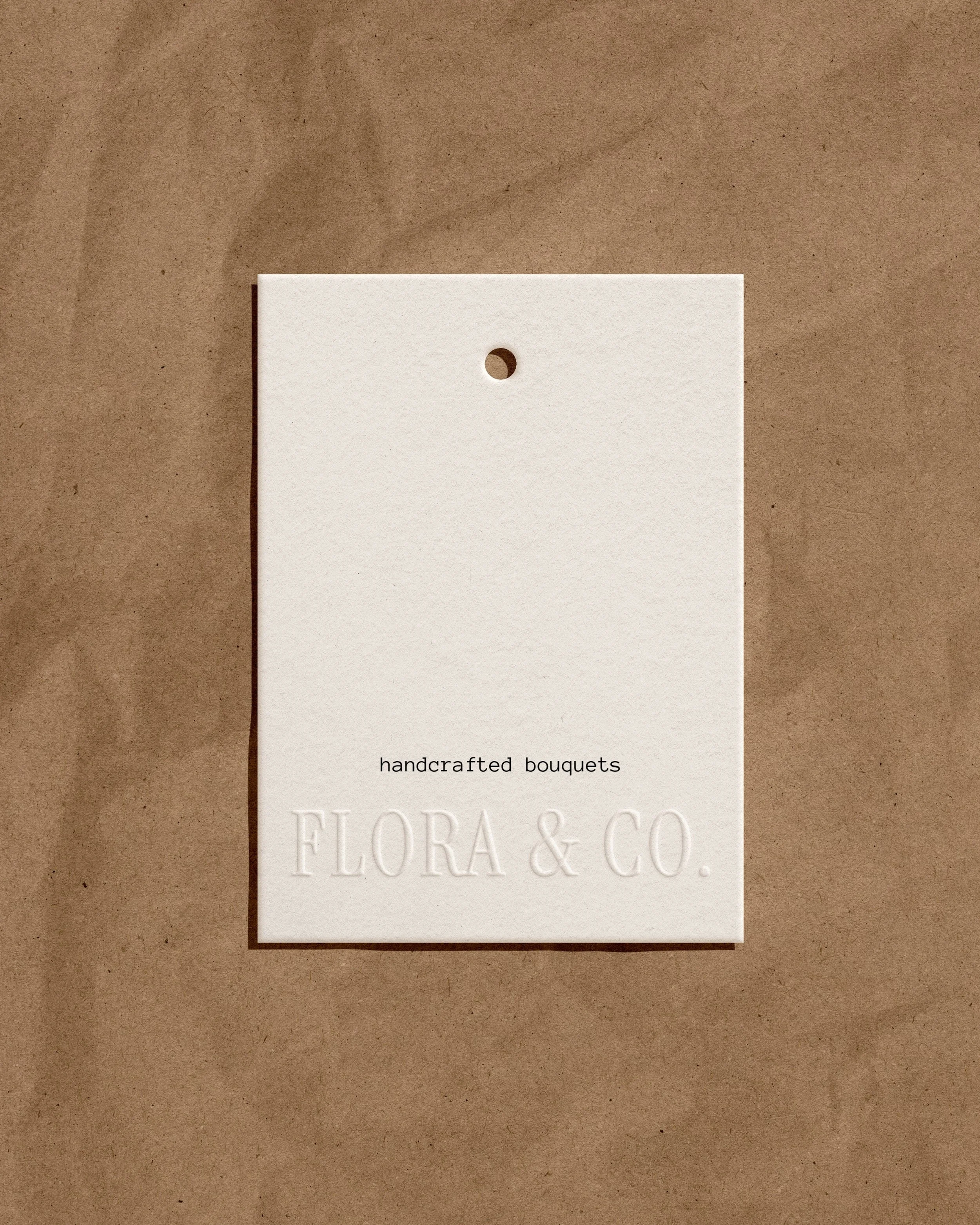 A white tag with a small hole at the top, placed on brown paper, labeled 'handcrafted bouquets' and 'FLORA & CO.'